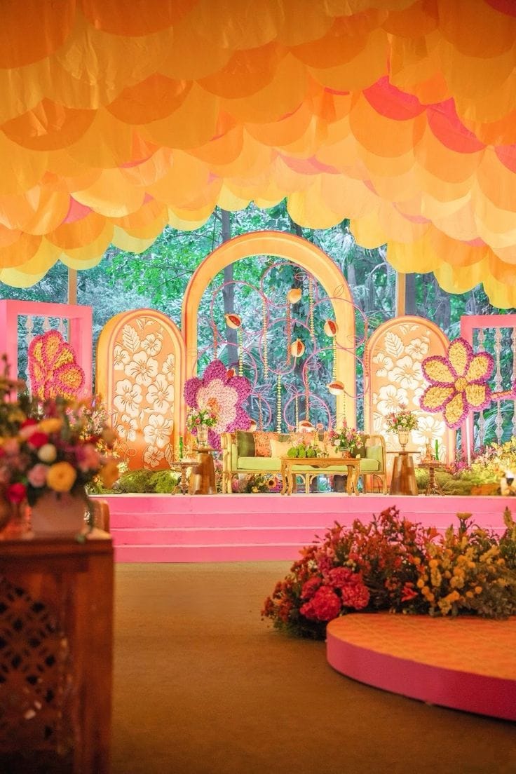 Orange and pink arched backdrop with floral cut-outs and a round stage platform by RAW Group